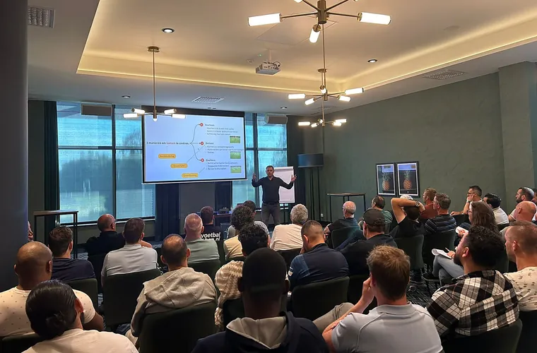 Ronnie Couwenberg staat met open armen voor een zaal voetbalcoaches, op het scherm achter hem staan drie manieren om kansen te creëren.